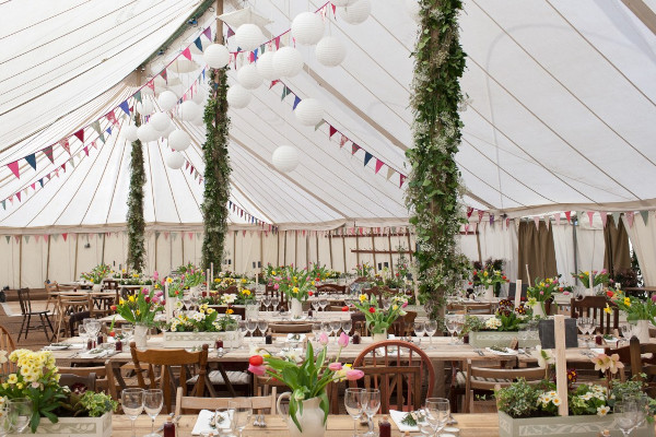 Interior of a traditional canvas marquee for a Spring wedding with mis-matched chairs and banqueting tables