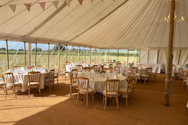 Interior of traditional marquee wedding with coir matting, round tables, banqueting chairs and bunting
