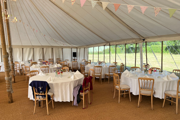 Interior of traditional marquee wedding with coir matting, round tables, banqueting chairs and bunting